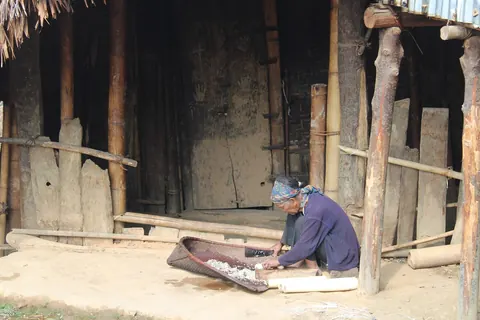 An elder working beside a traditional timber house