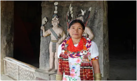 A woman in traditional attire and jewellery beside a carved pillar